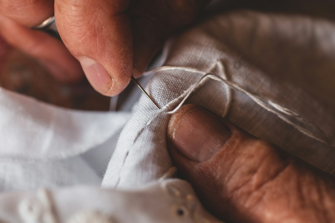A craftsman’s hands hand-stitching ivory bridal fabric
