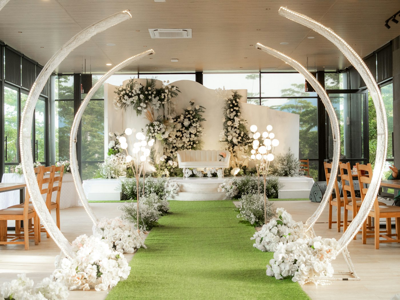Wedding venue dressed with white floral arches, a flower-lined aisle and a dais with a loveseat